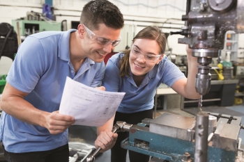 Engineer Instructing Female Apprentice On Use Of Drill